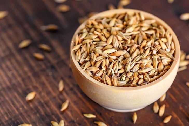 Barley grain in wooden bowl on wooden table