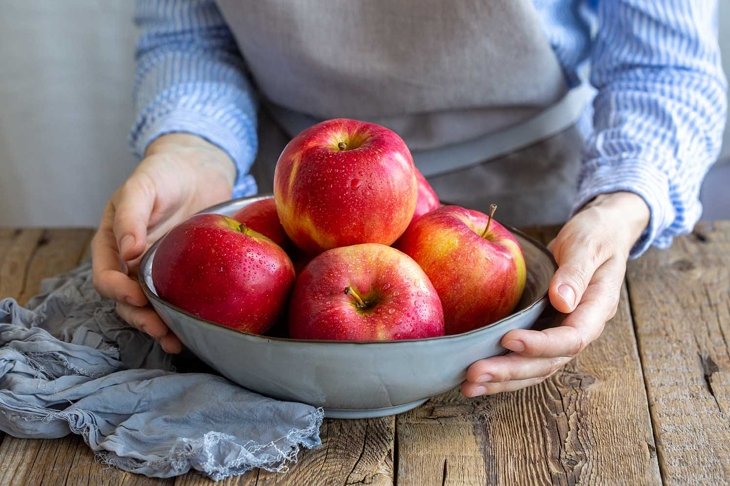 Apple saved. Apples washed in a bowl in the hands of the girl. A plate with red apples on a wooden table. Cooking food. Vegan. Food for vegetarians and vegans. Fresh fruits. Vitamins. Proper nutrition