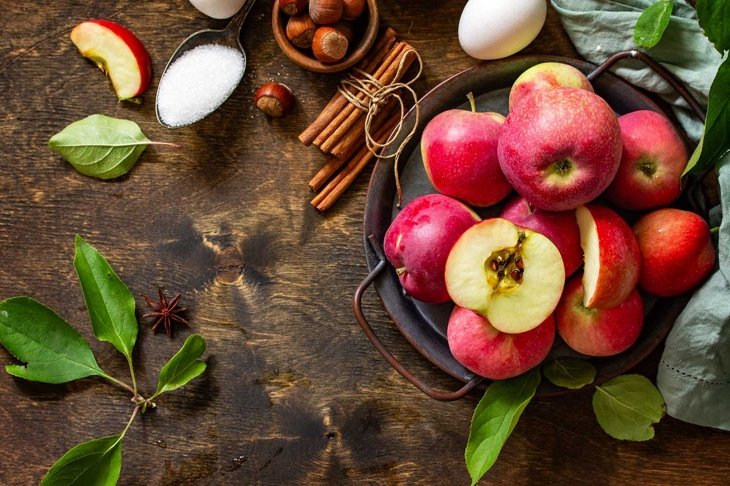 Apple baking seasonal concept. Ingredients for apple pie (red apple, flour, eggs, anise, sugar, hazelnut and cinnamon) on a rustic wooden table. Top view flat lay. Free space for your text.
