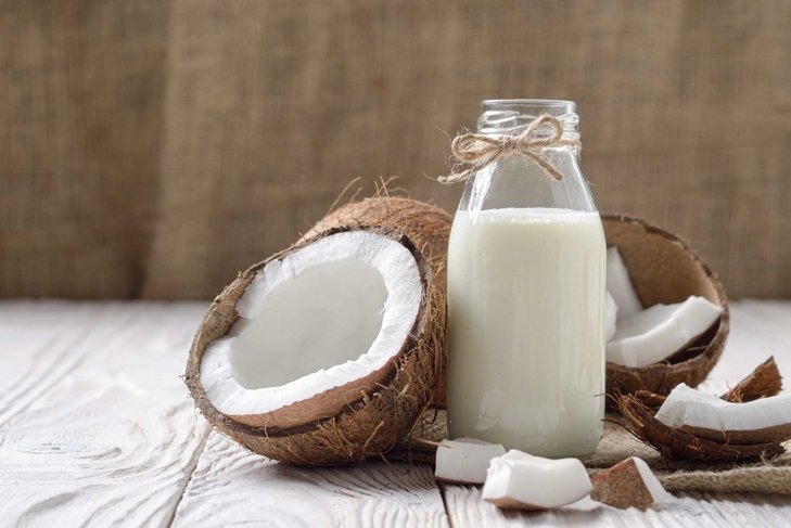 Glass bottle of milk or yogurt on hemp napkin on white wooden table with coconut aside