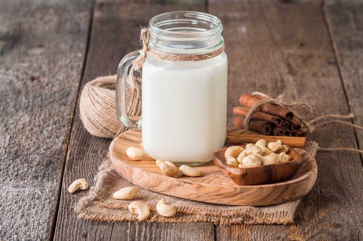 Cashew nut vegan milk non dairy in a glass jar with cashew nuts on wooden background