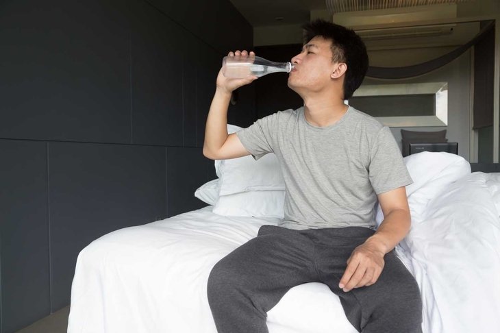 Drinking Water. Young asian man drinking water on bed