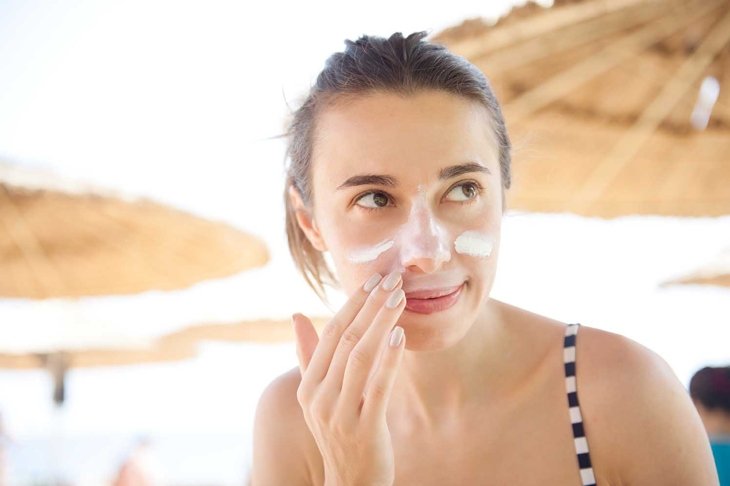beautiful woman smears face sunscreen at the beach for protection.
